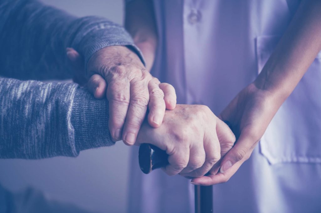 A nursing home care provider helps an elderly person with a cane.