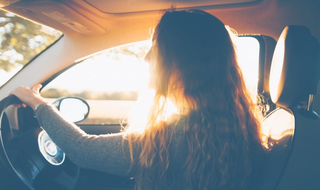 A woman driving a car as the sun shines in her hair.
