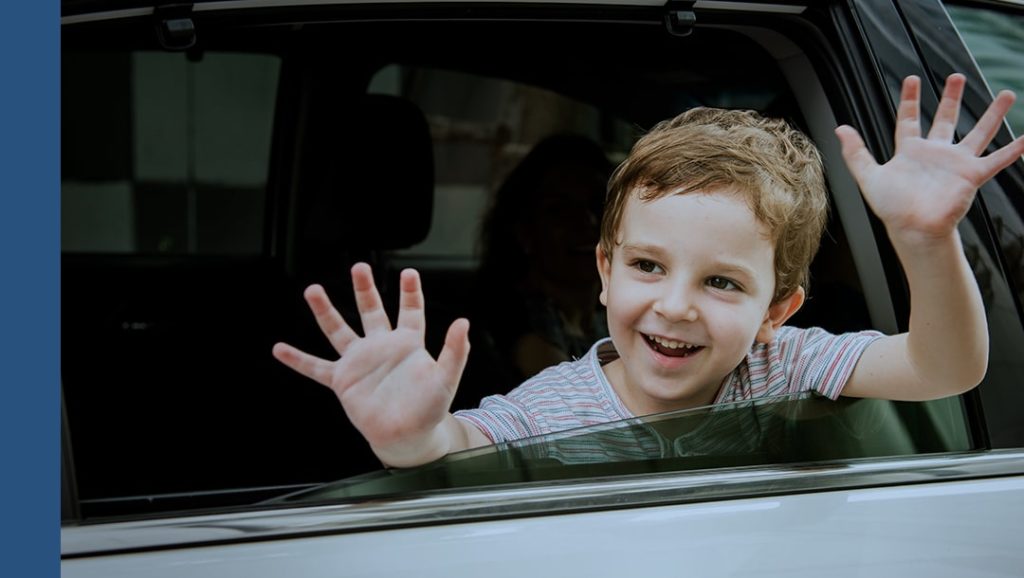 A child leaning out of a car window and waving.