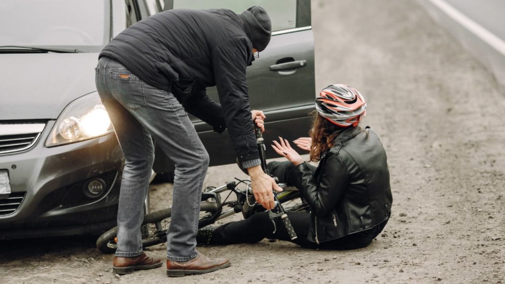 A driver helps up a bicyclist who was accidentally struck while biking on the road.